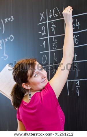 pretty young college student writing on the chalkboard/blackboard during a math class (color toned image; shallow DOF)