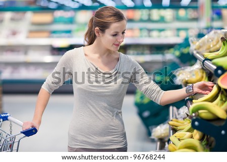 Beautiful youn woman shopping for fruits and vegetables in produce department of a grocery store/supermarket (shallow DOF; color toned image)