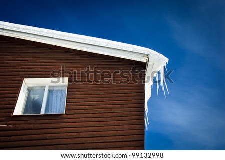 Winter/mountain concept: closeup of a wooden cottage roof covered with snow and icicles against blue sky