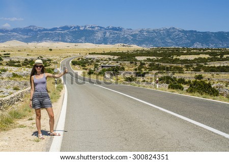 Young attractive woman hitchhiking along empty road