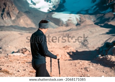 A young man travels, goes to the mountains in thermal underwear and with trekking poles, a hiker climbs to the top of the mountain, against the backdrop of red rocks and a glacier. 商業照片 © 
