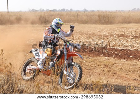BRITS, SOUTH AFRICA - July 11:  Africa-Offroad Racing Rally,  on July 11, 2015 at Koster, North West Province, South Africa.  Motorbiker thumbs up kicking up trail of dust.