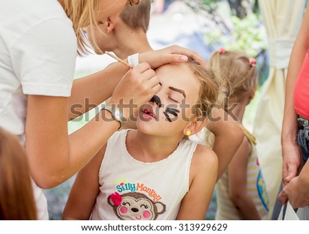 ZAPOROZHYE, UKRAINE - SEPTEMBER 5, 2015. Volunteer painting cat mask on girl face during family festival organized by Charity Fund Child`s Smile for citizens and Donetsk  refugees, financed by USAID