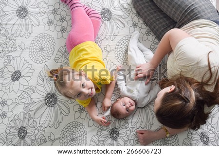 A mother and her four years old and three month old daughters lying playing on a bed.