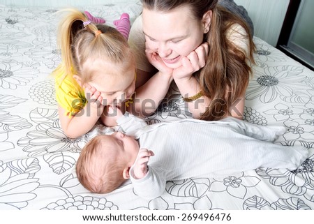 A portrait of a mother and her four years old and three month old baby daughters lying playing on a bed.