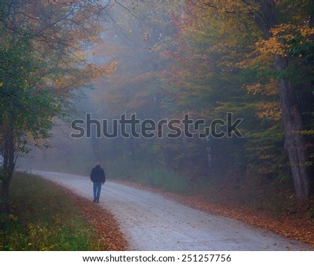 Man walking a misty back road in Vermont surrounded by the leaves and colors of autumn/Man Walking a Road in Vermont