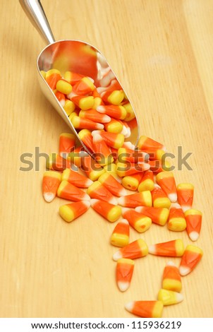 A scoop of candy corn spilling on a wood texture.