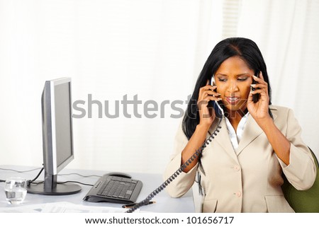Portrait of a young secretary talking on phone with two persons at the same time