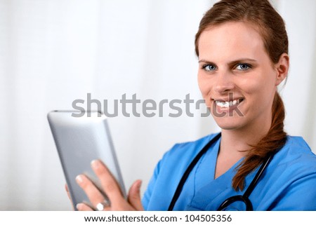 Close up portrait of a attractive blonde young nurse smiling with a tablet PC at hospital workplace