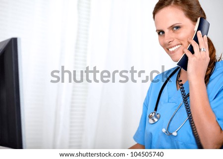 Portrait of a beautiful blonde woman on blue medical uniform waiting on phone at hospital