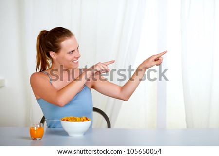 Portrait of a charming youmg woman eating meal and pointing with the two hands to the right
