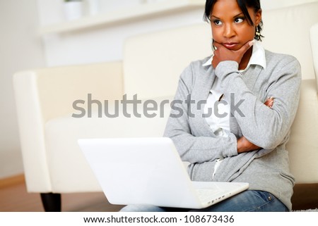 Portrait of a reflective young woman sits on the floor in front of her laptop at home indoor