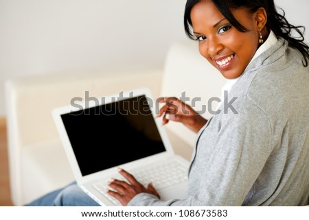 Portrait of a beautiful black female working on laptop on sofa at home while is looking to you