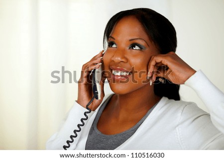 Portrait of a lovely black woman smiling and conversing on phone at home indoor while looking up