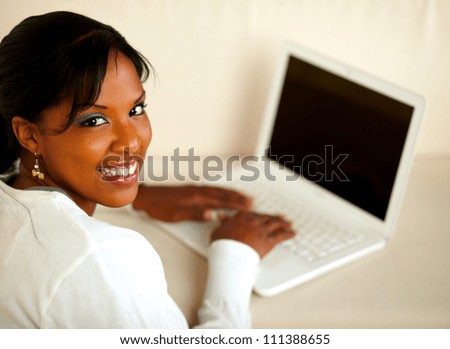 Portrait of a stylish female looking at you while working on laptop at home indoor. With copyspace