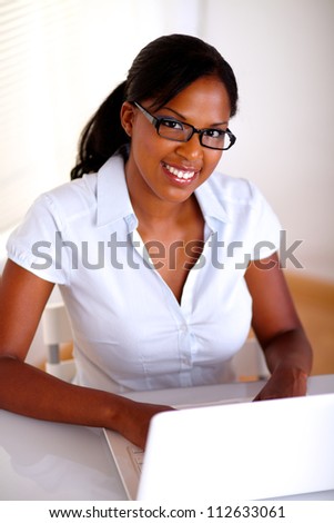 Afro-american secretary looking at you in front of her laptop at workplace