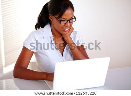 Top view of a charming young black woman with glasses working on laptop at workplace - copyspace