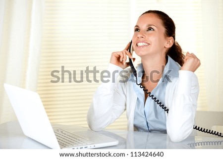 Happy and excited young woman speaking on phone at office in front of laptop