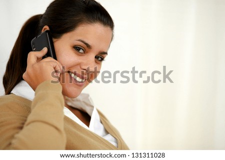 Portrait of a smiling latin young female speaking on cellphone while is looking at you