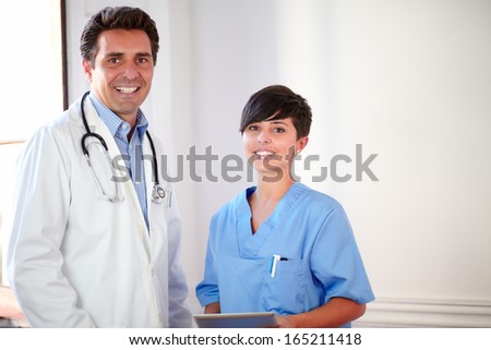 Portrait of a handsome latin doctor and beautiful nurse on medical uniform standing and holding a tablet pc - copyspace