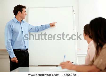 Portrait of a handsome adult businessman pointing and looking at whiteboard while standing in front of hispanic women on office - copyspace
