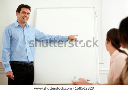 Portrait of an attractive businessman pointing at whiteboard while standing and looking at young female colleagues on office - copyspace