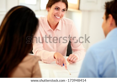 Portrait of lovely financial advisor woman at meeting with young couple while smiling and sitting at bank office