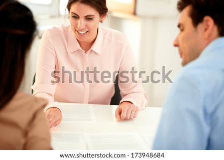 Portrait of adult financial advisor lady explaining an application form to a young couple while listen and sitting on office desk
