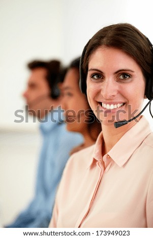 Portrait of beautiful female operator on pink shirt with headphones smiling at you while sitting on workplace -