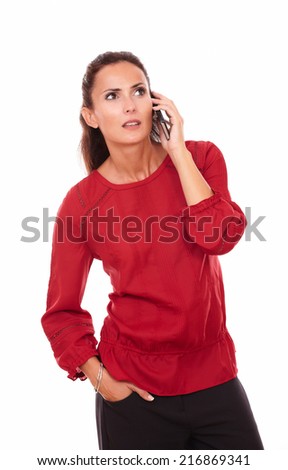 Portrait of surprised young lady on red shirt talking on her cellphone while standing on isolated white background - copyspace