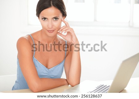 Sophisticated woman in blue blouse working on the computer while looking at you in her room