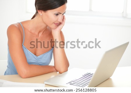 Latin brunette woman in blue blouse studying on her laptop while sitting at her home