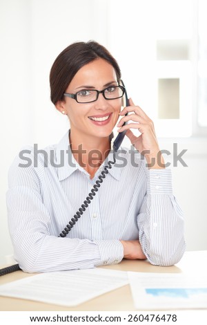 Corporate secretary with glasses happily talking on the phone while smiling in her office