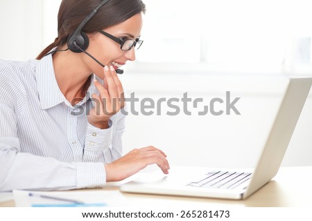 Cheerful receptionist in blue blouse conversing on her headset while smiling