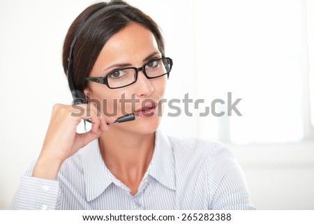 Pretty woman in blue blouse conversing on headphones while looking at you, taken closeup