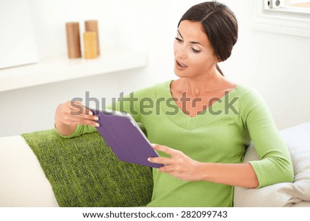 Waist up portrait of a surprised woman looking at a tablet with her mouth open