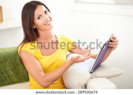 Attractive young woman in yellow tank top pointing at a tablet while sitting indoors