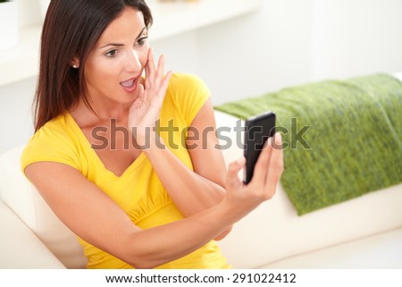 Surprised woman of caucasian ethnicity using a cell phone while sitting indoors - copy space