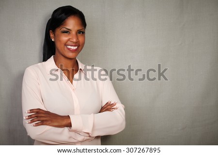 Charismatic female in button down shirt smiling with arms crossed against grey background