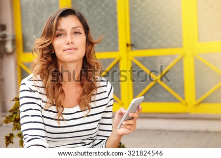 Caucasian lady looking at the camera while sitting and holding mobile phone