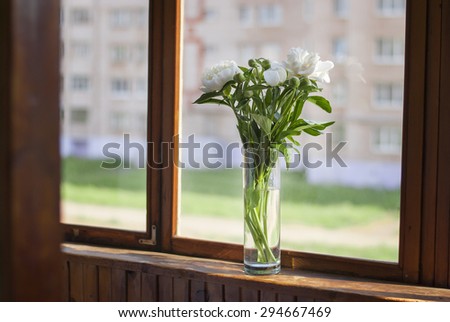 Bouquet of peonies in a glass vase on the window. The sun's rays on a wooden window sill, blurred background.