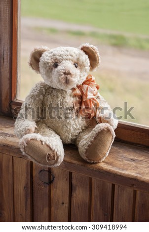 Vintage handmade Teddy Bear with bow sits on balcony window.