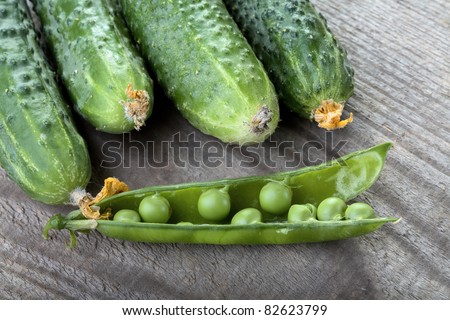 Green cucumbers and peas pod on a table from unplaned boards