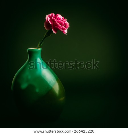 Pink carnation flower in a green vase on black background
