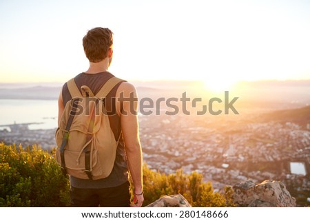 Rearview of a young man with a backpack watching the sunrise from a nature trail above the city
