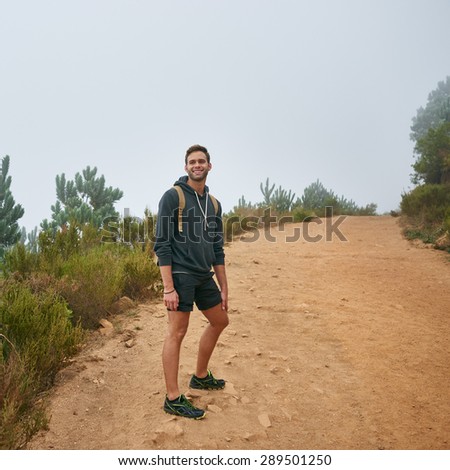 Full length shot of a young male hiker smiling back at the camera while on a nature trail on a misty morning