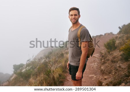 Portrait of a handsome young hiker smiling at the camera on a mountain trail on a misty morning