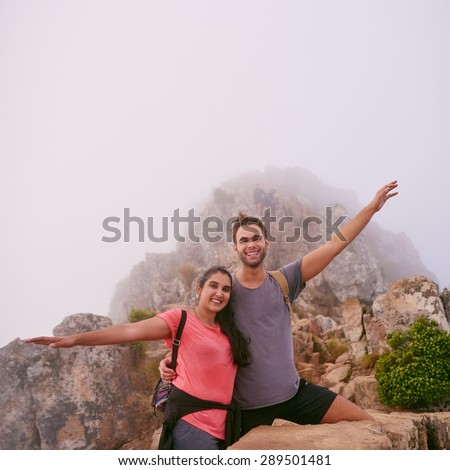 Portrait of two friends smiling together with their arms outstretched on a mountain nature trail that they have climbed together