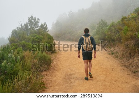 Rear view of a young man walking on a nature trail away from the camera with the natural surrounds disappearing into morning mist