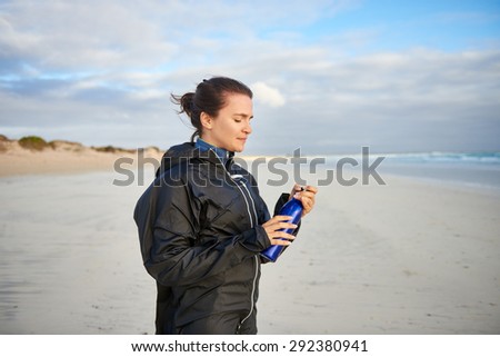 Young woman holding a water bottle while on a walk on the beach in winter